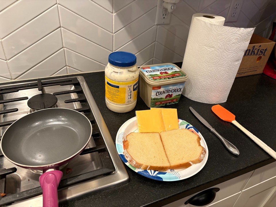 ingredients and tools for grilled-cheese making. Includes mayo, bread, cheese, butter, and standard kitchen equipment.